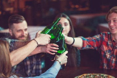 Arkadaşlar bir barda bir içki sahip, onlar bira ve pizza ile ahşap bir masada oturuyor.