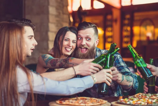 Amigos tomando una copa en un bar, están sentados en una mesa de madera con cervezas y pizza . —  Fotos de Stock