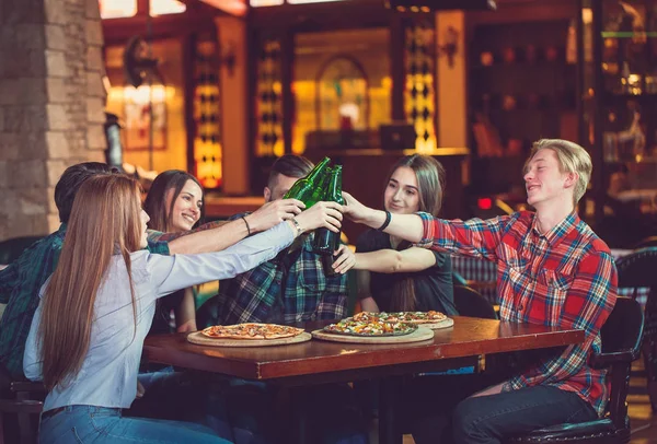 Amigos tomando una copa en un bar, están sentados en una mesa de madera con cervezas y pizza . —  Fotos de Stock
