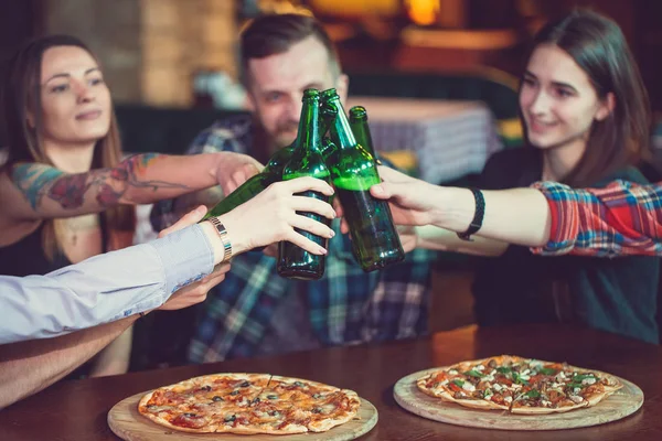 Amigos tomando una copa en un bar, están sentados en una mesa de madera con cervezas y pizza . —  Fotos de Stock