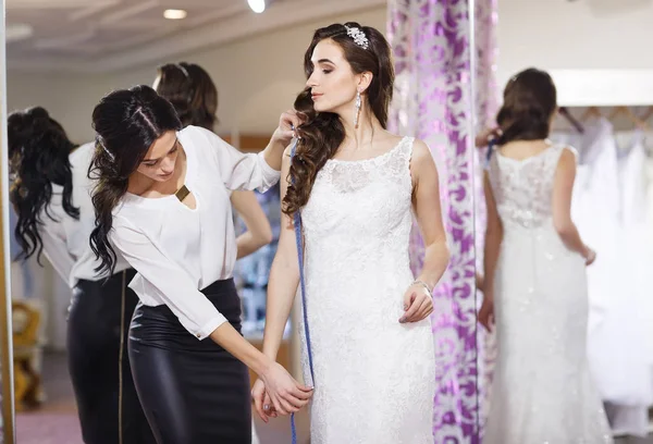 Kobieta próbuje na sukni ślubnej w sklepie z asystentem kobiet. — Zdjęcie stockowe