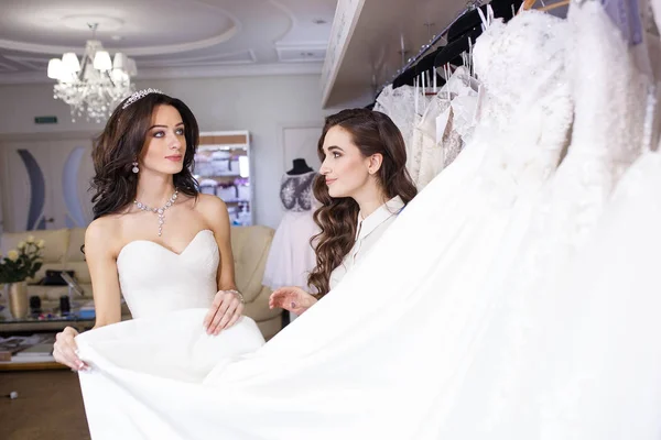 Frau probiert Hochzeitskleid im Geschäft mit weiblicher Assistentin an. — Stockfoto