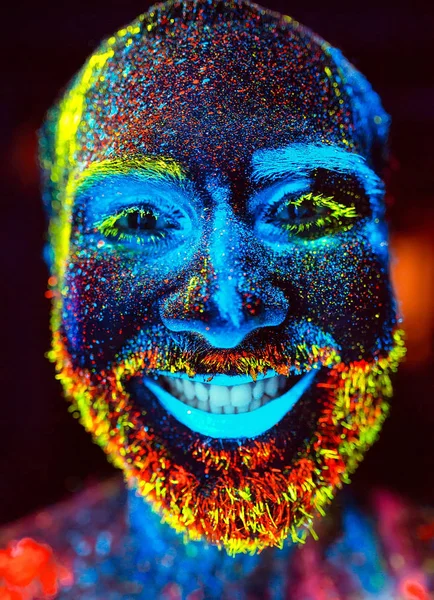 Conceito. Um homem barbudo sorri. Retrato de um homem barbudo pintado em pó fluorescente . — Fotografia de Stock