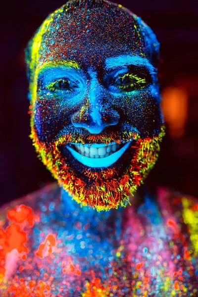 Concepto. Un hombre barbudo sonríe. Retrato de un hombre barbudo pintado en polvo fluorescente . — Foto de Stock