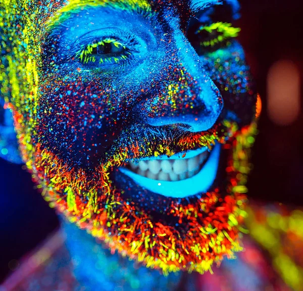 Concepto. Un hombre barbudo sonríe. Retrato de un hombre barbudo pintado en polvo fluorescente . — Foto de Stock