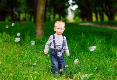 Küçük çocuk parkta sabun köpüğüyle oynuyor..