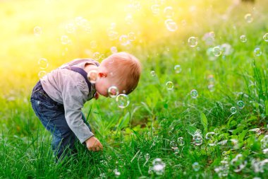 Küçük çocuk parkta sabun köpüğüyle oynuyor.