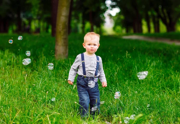Küçük çocuk parkta sabun köpüğüyle oynuyor..