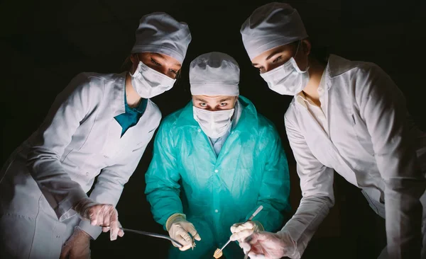 Der Chirurg führt eine Operation in einem dunklen Raum durch. — Stockfoto