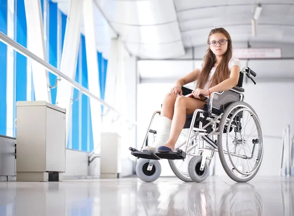 Uma rapariga numa cadeira de rodas está a ler um livro. Paciente em cadeira de rodas no corredor do hospital — Fotografia de Stock