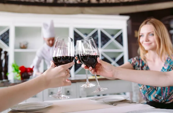 Young people in a restaurant drinking wine in the background a cook prepares