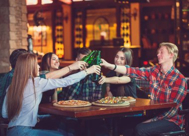 Arkadaşlar bir barda bir içki sahip, onlar bira ve pizza ile ahşap bir masada oturuyor