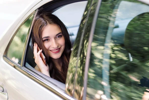 Una joven está sentada en el asiento trasero de un coche y está hablando por teléfono. . — Foto de Stock