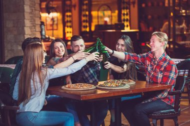 Arkadaşlar bir barda bir içki sahip, onlar bira ve pizza ile ahşap bir masada oturuyor