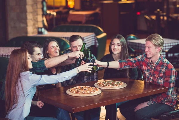 Amigos tomando una copa en un bar, están sentados en una mesa de madera con cervezas y pizza —  Fotos de Stock