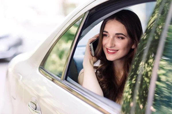 Una joven está sentada en el asiento trasero de un coche y está hablando por teléfono. . — Foto de Stock