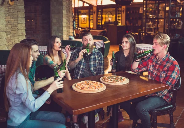 Friends having a drinks in a bar, They are sitting at a wooden table with beers and pizza