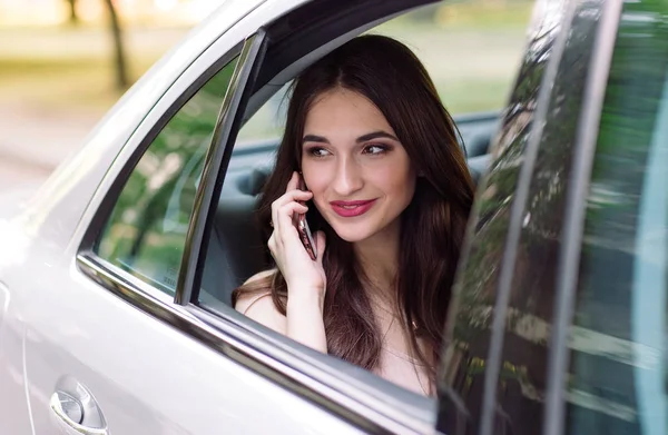 A young girl is sitting in the back seat of a car and is talking on the phone. — Stock Photo, Image