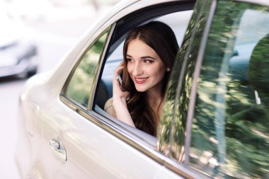 Genç bir kız bir arabanın arka koltuğunda oturan ve telefonda konuşuyor.