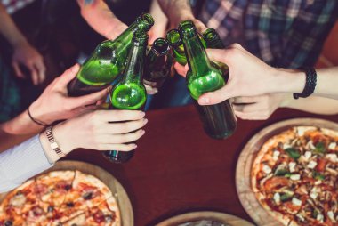 Arkadaşlar bir barda bir içki sahip, onlar bira ve pizza ile ahşap bir masada oturuyor