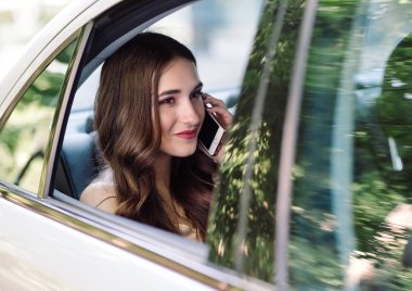 Genç bir kız bir arabanın arka koltuğunda oturan ve telefonda konuşuyor.