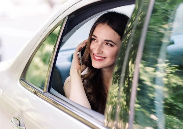 Una joven está sentada en el asiento trasero de un coche y está hablando por teléfono. . — Foto de Stock