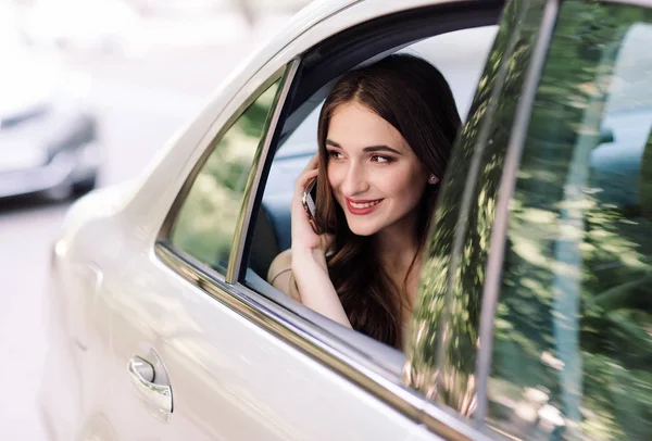 Una joven está sentada en el asiento trasero de un coche y está hablando por teléfono. . — Foto de Stock
