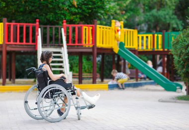 Kırık bir bacak bir kızla Bahçesi önünde tekerlekli sandalyede oturur.
