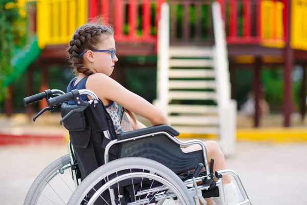 Девушка со сломанной ногой сидит в инвалидном кресле перед детской площадкой . — стоковое фото