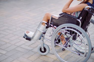 Bacağı kırık bir kız tekerlekli sandalyede oturuyor.