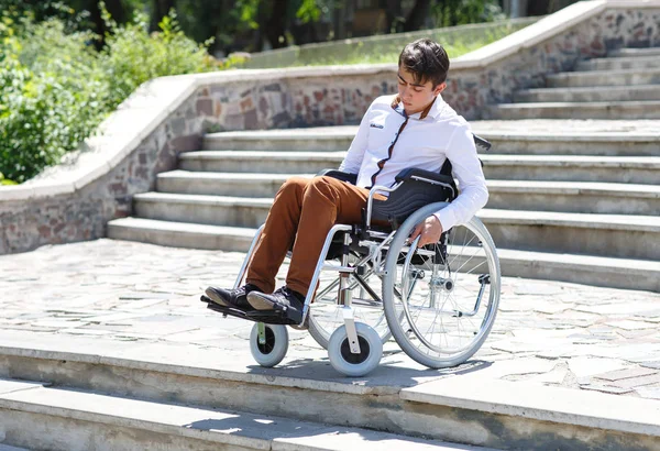 Um jovem em uma cadeira de rodas que não pode descer as escadas . — Fotografia de Stock