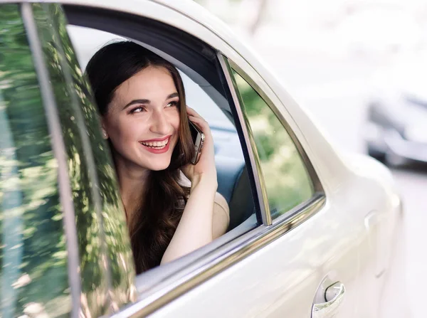 Una joven está sentada en el asiento trasero de un coche y está hablando por teléfono. — Foto de Stock