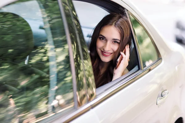 Una joven está sentada en el asiento trasero de un coche y está hablando por teléfono. — Foto de Stock