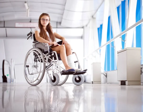 Uma rapariga numa cadeira de rodas está a ler um livro. Paciente em cadeira de rodas no corredor do hospital . — Fotografia de Stock