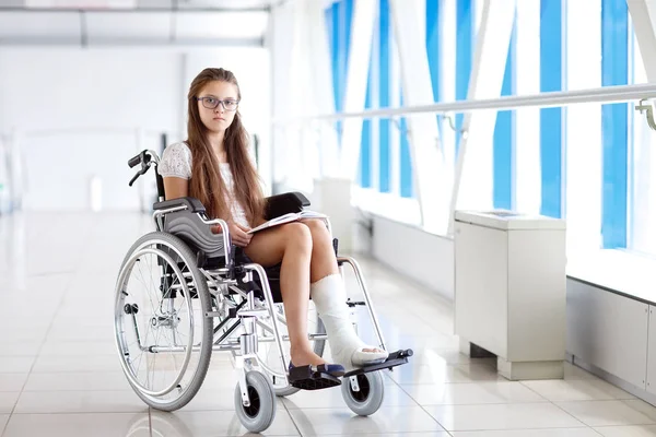 Uma rapariga numa cadeira de rodas está a ler um livro. Paciente em cadeira de rodas no corredor do hospital . — Fotografia de Stock