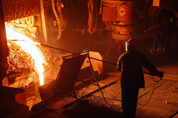 Plant for the production of steel. An electric melting furnace. Factory worker takes a sample for metal