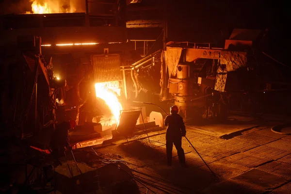 Завод з виробництва сталі. Електрична піч для плавлення. Заводський робітник бере зразок для металу — стокове фото