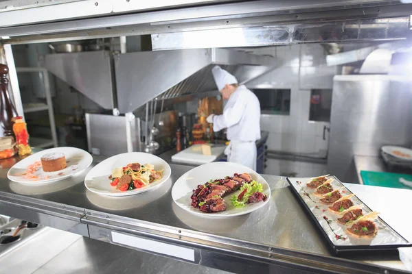 The distribution table in the kitchen of the restaurant. the chef prepares a meal on the background of the finished dishes. — Stock Photo, Image