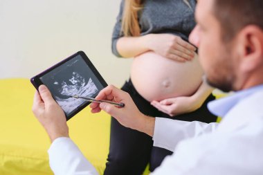 Jinekolog hamile kadına yankı fotoğrafı gösteriyor.