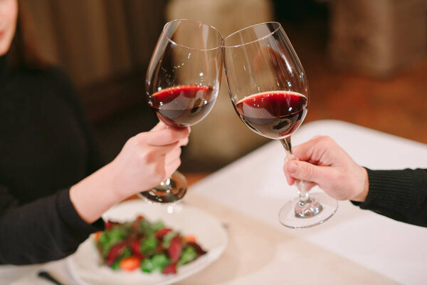 Man and woman drinking red wine. In the picture, close-up hands with glasses