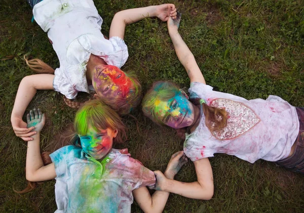 Çocuklar çimlerin üzerinde yatar. Holi festivalinin renklerine boyanmış çocuklar çimlerin üzerinde yatıyor.