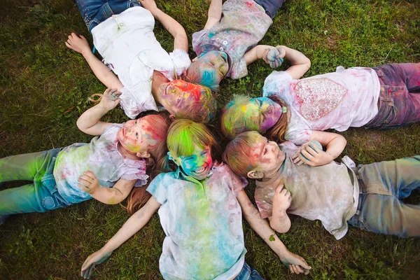 Children lie on the grass. Children painted in the colors of Holi festival lie on the grass. — Stock Photo, Image