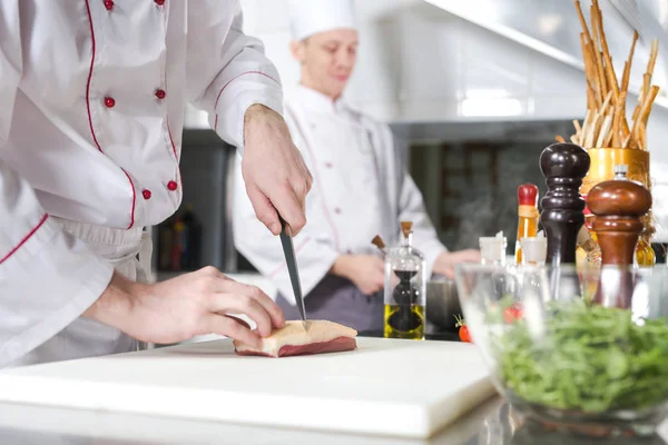 Chef schneidet Fleisch auf Schneidebrett, professioneller Koch hält Messer und schneidet Fleisch im Restaurant. — Stockfoto