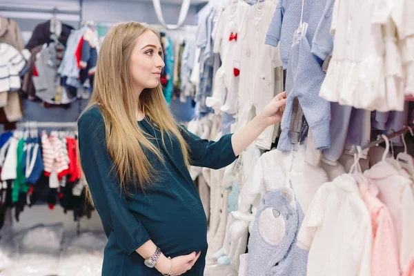 Беременная женщина выбирает одежду для детей в магазине — стоковое фото
