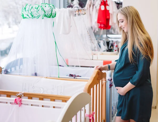 Fille enceinte choisit un lit bébé dans le magasin — Photo
