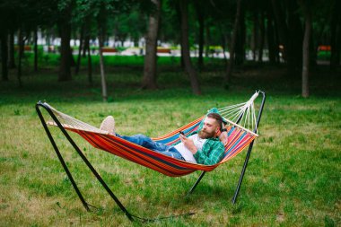 bir hamakta sallanan beyaz onun cep telefonu bir uygulama kullanarak adam.