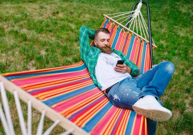 bir hamakta sallanan beyaz onun cep telefonu bir uygulama kullanarak adam.