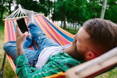 bir hamakta sallanan beyaz onun cep telefonu bir uygulama kullanarak adam.