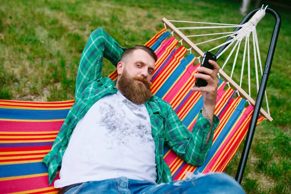 Mann schwingt mit einer App auf seinem Handy in einer Hängematte. — Stockfoto