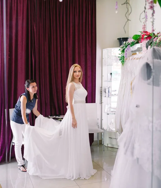 Mujer probándose el vestido de novia en una tienda con las mujeres asistente . — Foto de Stock